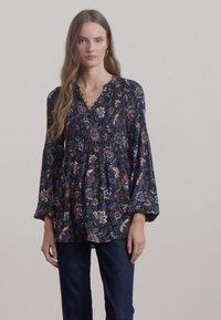 Tamsi gėlių palaidinė su V formos iškirpte, ilgomis skraistėmis ir raukšlėmis priekyje, pasižyminti mėlynų, raudonų ir baltų raštų mišiniu tamsiai mėlyname fone.