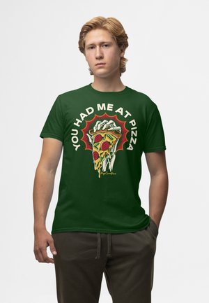 Grøn bomulds T-shirt med et grafisk motiv af en hånd, der holder en skive pepperoni-pizza, omgivet af teksten "DU FIK MIG TIL AT ELSKE PIZZA."