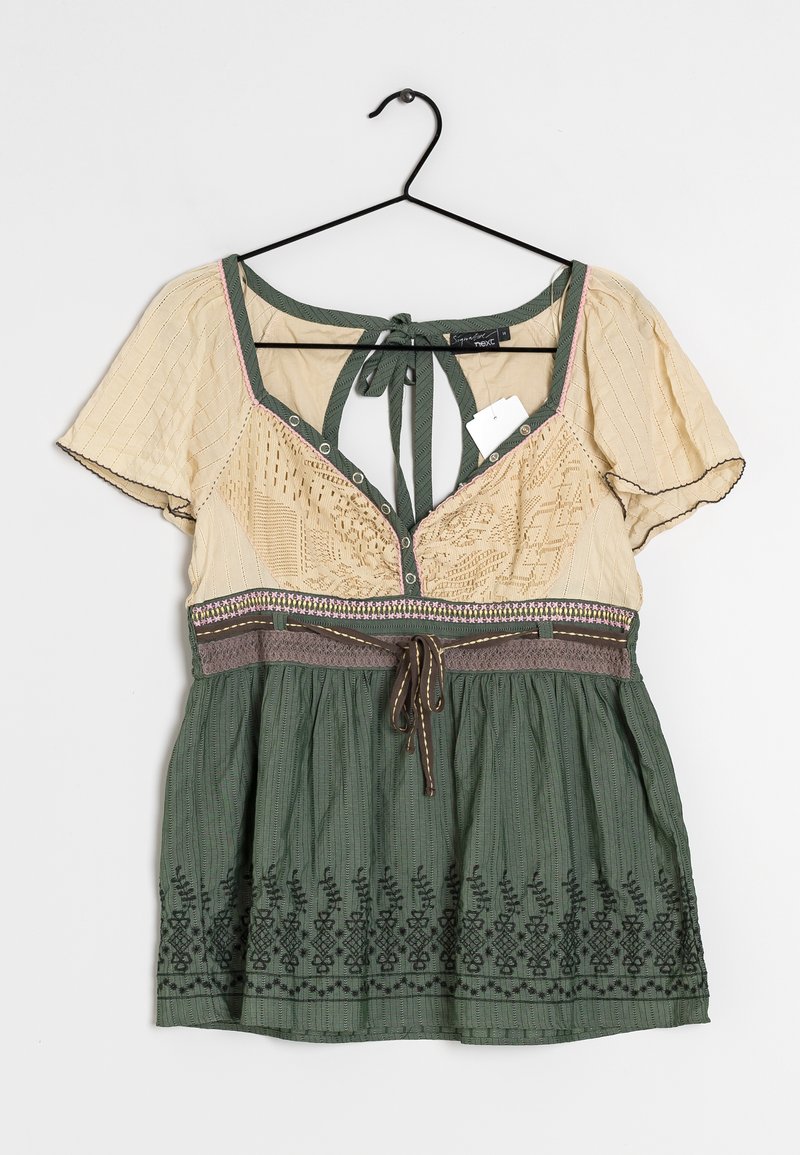 Blouse beige et verte avec motif floral brodé, manches courtes, lien à nouer dans le dos et fermeture par bouton sur un tissu texturé sur le haut.