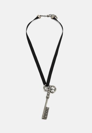 Strieborný pendant vo vintage štýle vo forme kľúča, na ktorom je vygravírované "Moschino", zavesený na čiernom textilnom náhrdelníku s kovovým zapínaním a nastaviteľným reťazcom.