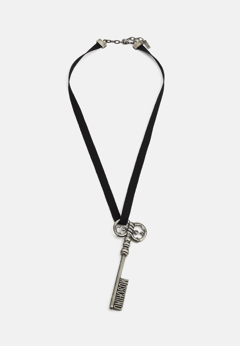 Pingente de chave antiga de prata com o gravado "Moschino" numa corrente de tecido preto com fecho metálico e corrente ajustável.