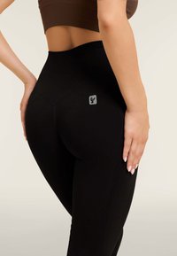 Leggings neri a vita alta realizzati in tessuto elasticizzato, con un motivo testurizzato e un piccolo logo grigio sul lato. Design liscio e aderente.