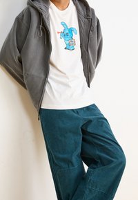Gray hooded sweatshirt over a white T-shirt featuring a blue cartoon bunny, paired with teal corduroy pants. Smooth textures and relaxed fit.