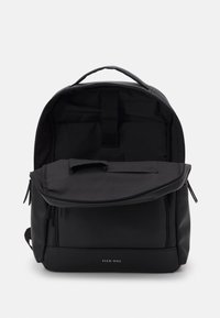 Sac à dos noir en matériau synthétique, doté d'un compartiment principal zippé, d'une poche intérieure et d'une poignée de transport supérieure. Design minimaliste.
