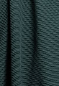 Gestructureerde stof in een diep groene kleur met een roosterachtig patroon. Zacht materiaal met duidelijke oppervlakdetails.