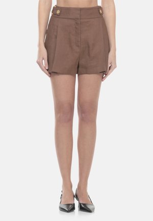 Short marroni a vita alta su misura con pieghe e dettagli con bottoni, indossati con tacchi neri a punta su gambe nude.