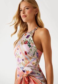 Blommönstrad halterneck-top med pastellfärger, en figursydd design och en sidoknutdetalj, tillverkad av lättviktig tyg med en mjuk textur.