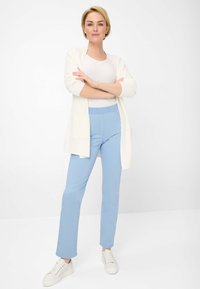 Witte langemouwen cardigan over een lichtgrijs topje en lichtblauwe broek. Witte sneakers, slim fit, gladde stof, geen zichtbare patronen of hardware.