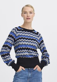 Åtsittande tröja med zigzag-mönster i blått, svart och grått. Långa ärmar med ribbade mudd och en helsvart midja. Stickad textur.
