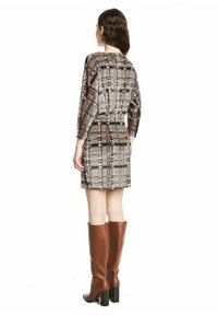 Korte mouwen, aansluitend jurk in een gestructureerd zwart en beige patroon met oranje accenten, gecombineerd met bruin leren laarzen tot de knie.