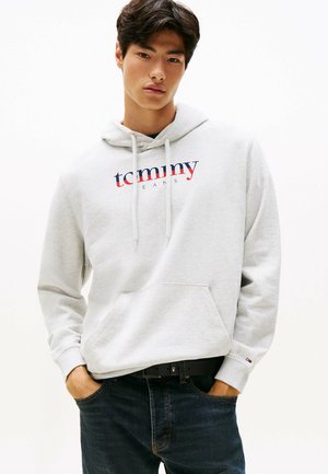 Grå hættetrøje med en frontlomme, der har "tommy" i rød og blå over "JEANS." Parret med mørk denim jeans og et sort bælte.