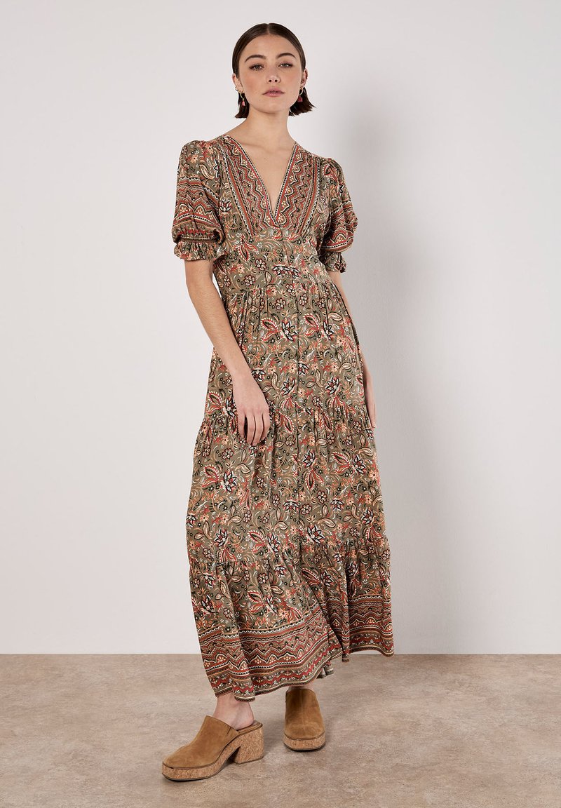 Robe longue à motifs dans des tons terreux, avec des manches bouffantes, un décolleté en V profond et une jupe à volants. Portée avec des sabots épais à talons en tan.