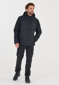 Sort puffjakke med en tætsiddende design, med hætte, lynlås foran og strukturerede paneler. Matched med sorte cargo bukser og støvler.
