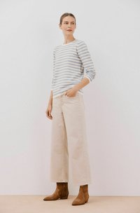 Pasiasty longsleeve w kolorze niebiesko-białym, w połączeniu z beżowymi spodniami w szerokim kroju i brązowymi botkami za kostkę, na neutralnym tle.