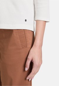 Top bianco a costine con maniche a tre quarti, dotato di un piccolo logo nero sull'orlo, abbinato a pantaloni marroni con tasca laterale.