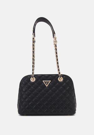 Sac à main noir matelassé avec des anses en chaîne dorée et une plaque triangulaire avec le logo Guess au centre avant.