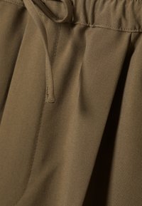Khakifarbe mit glatter Textur, ausgestattet mit Kordelzug und Falten-Design. Das Material wirkt leicht und langlebig.
