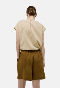 Haut beige à manches courtes avec un détail de bouton dans le dos, associé à un short ample en olive foncé doté d'une taille élastique et de poches latérales.