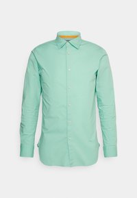 Camicia verde chiaro a maniche lunghe con colletto a bottoni, con un accento giallo all'interno del colletto e chiusura frontale con bottoni.