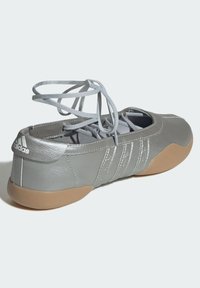 Lys grå Adidas ballettsko med omslutningssnøring og gummisåle, designet for innendørs bruk og danseaktiviteter.