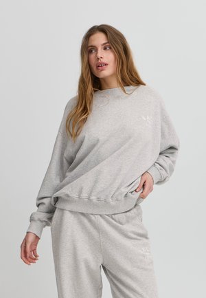 Sweatshirt gris à coupe détendue, avec des poignets et un ourlet côtelés. Présente un discret logo sur la poitrine, assorti avec un pantalon de survêtement gris.