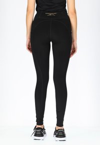 Zwarte sportleggings met een hoge tailleband, voorzien van een zachte textuur, stiksels en een logo nabij de tailleband.