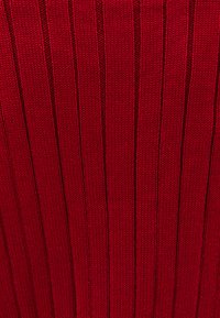 Punainen neulottu kangas, jossa on pystysuora ribbineuloskuvio, vuorotellen koholla ja syvällä olevia viivoja. Pehmeä materiaali, jossa on lievä kiilto.