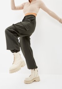 Suéter corto de punto ribeteado beige combinado con pantalones cargo verde oscuro y botas de combate beige gruesas con suelas acanaladas y cordones.