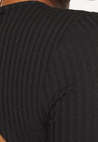 Svart ribbad stickad topp med en texturerad yta och figurnära design, som visar horisontella ränder längs tyget.