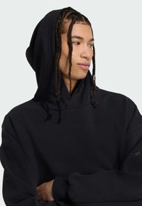 Sort bomulds hoodie med stor hætte, løs pasform og lange ærmer. Har flettet hår, minimalistisk design og ribbede manchetter.