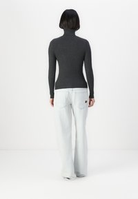 Suéter de cuello alto de canalé en color carbón combinado con jeans de pierna ancha en azul claro. El suéter presenta una silueta ajustada y mangas largas.