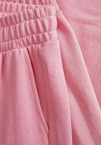 Roza tkanina z gladko teksturo, ki ima elastičen pas. Tkanina ima subtilen rebrast vzorec z nabranimi detajli.