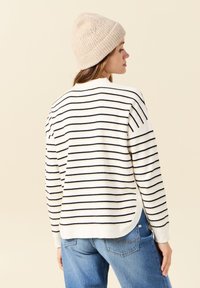 Pull rayé blanc et marine, avec un col rond et des poignets côtelés. Associé à un jean en denim bleu clair et un bonnet en tricot beige.