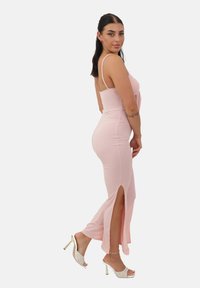 Vestido maxi de color rosa claro, con relieve, tirantes finos y hendiduras laterales. Lleva unos tacones abiertos acolchados blancos. Textura suave, diseño ajustado.