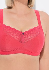 Růžová texturovaná podprsenka s krajkovým detailem nahoře, se středovou mašlí a nastavitelnými špagetovými ramínky. Výrazný vzor s puntíky.