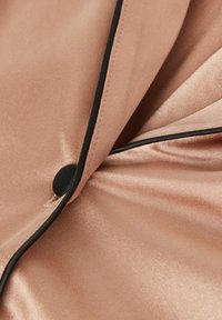 Satin tyg i mjuk rosa med svarta kantdetaljer och en svart knapp vid skärningspunkten av vikningar, vilket visar en slät textur och lyster.