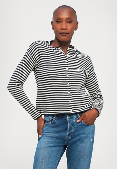 Schwarz-weißer gestreifter Langarm-Cardigan mit Knopfverschluss, geripptem Textur und lässiger Passform, kombiniert mit blauen Jeans.
