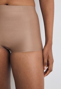 Nahtlose beiger Boyshorts aus glattem Material, mit hohem Bund und minimalistischem Design, teilweise am Körper eines Models präsentiert.