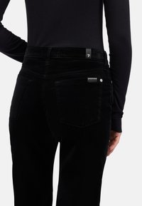 Pantaloni in velluto nero con vita alta, dotati di due tasche posteriori, dettaglio logo discreto e trama liscia. Il design è aderente.