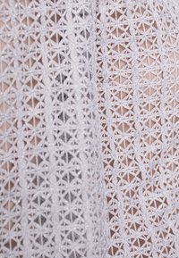 Material din dantelă albă cu modele geometrice, având forme complexe de stele și o strălucire subtilă datorată paietelor încorporate.