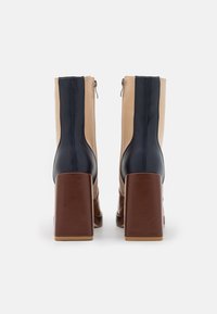 Bottes à talons hauts présentant un design bicolore en cuir bleu marine et beige, avec un talon carré marron et une fermeture éclair à l'arrière.