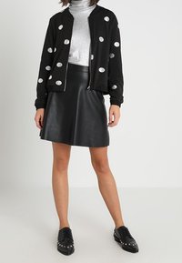Giacca bomber nera con pois bianchi, dolcevita lucida argentata, gonna di pelle nera e scarpe nere con borchie argentate.