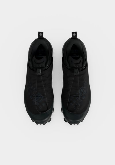 Μαύρα αθλητικά παπούτσια χωρίς κορδόνια με ελαστικά κλείσιμο, ανθεκτικές σόλες και θηλιές στη φτέρνα, σε άποψη από πάνω σε λευκό φόντο.