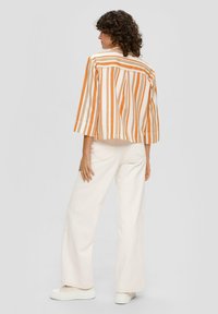 Gestreepte jas in oranje en wit, vierkante ontwerp met driekwartmouwen. Gepaard met hoge taille, wijde crèmekleurige broek en witte sneakers.