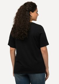 Černé bavlněné tričko s krátkým rukávem a volným střihem, s jednoduchým kulatým výstřihem, nošené s tmavě modrými džíny.