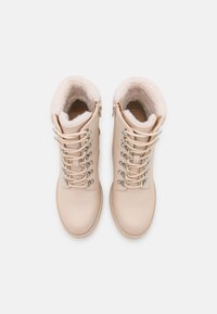 Beige turistické boty s umělou kožešinou, kovovými očky a šněrovacím designem. Hladký kožený svršek a plochá gumová podešev.