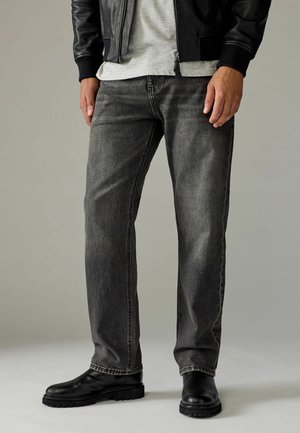 Donkergrijze jeans met een recht gesneden ontwerp, voorzien van subtiele vervaging, gestikte details en een versleten textuur, gecombineerd met zwarte leren laarzen.