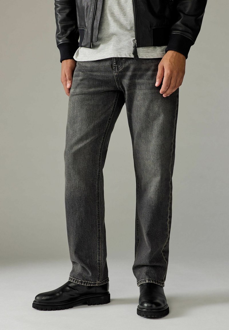 Donkergrijze jeans met een recht gesneden ontwerp, voorzien van subtiele vervaging, gestikte details en een versleten textuur, gecombineerd met zwarte leren laarzen.