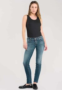 Débardeur noir, jeans skinny bleus, mocassins noirs. Design ajusté avec une texture lisse. Les jeans sont dotés d'une fermeture à bouton et à fermeture éclair.