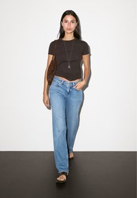 Tmavě hnědé přiléhavé tričko, světle modré rovné džíny a černé žabky, doplněné hnědou perlovou kabelkou a stříbrným náhrdelníkem.